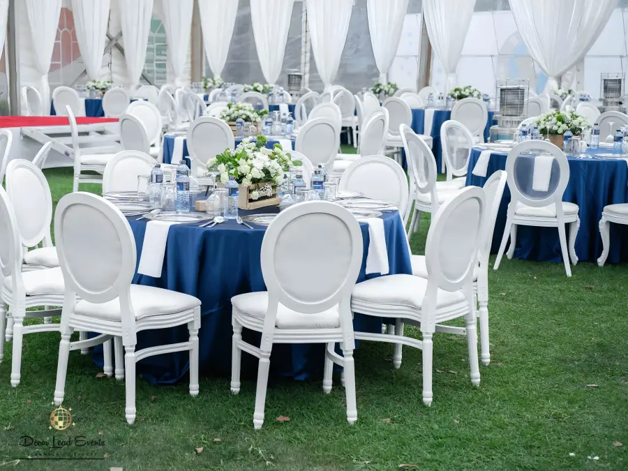 Another angle of the tent interior showing the layout of round tables with navy blue linens and white chairs on a green lawn.