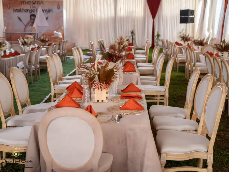 Boho-themed event setup featuring long tables with beige linens, rust-colored napkins, dried floral centerpieces, and beige upholstered chairs.