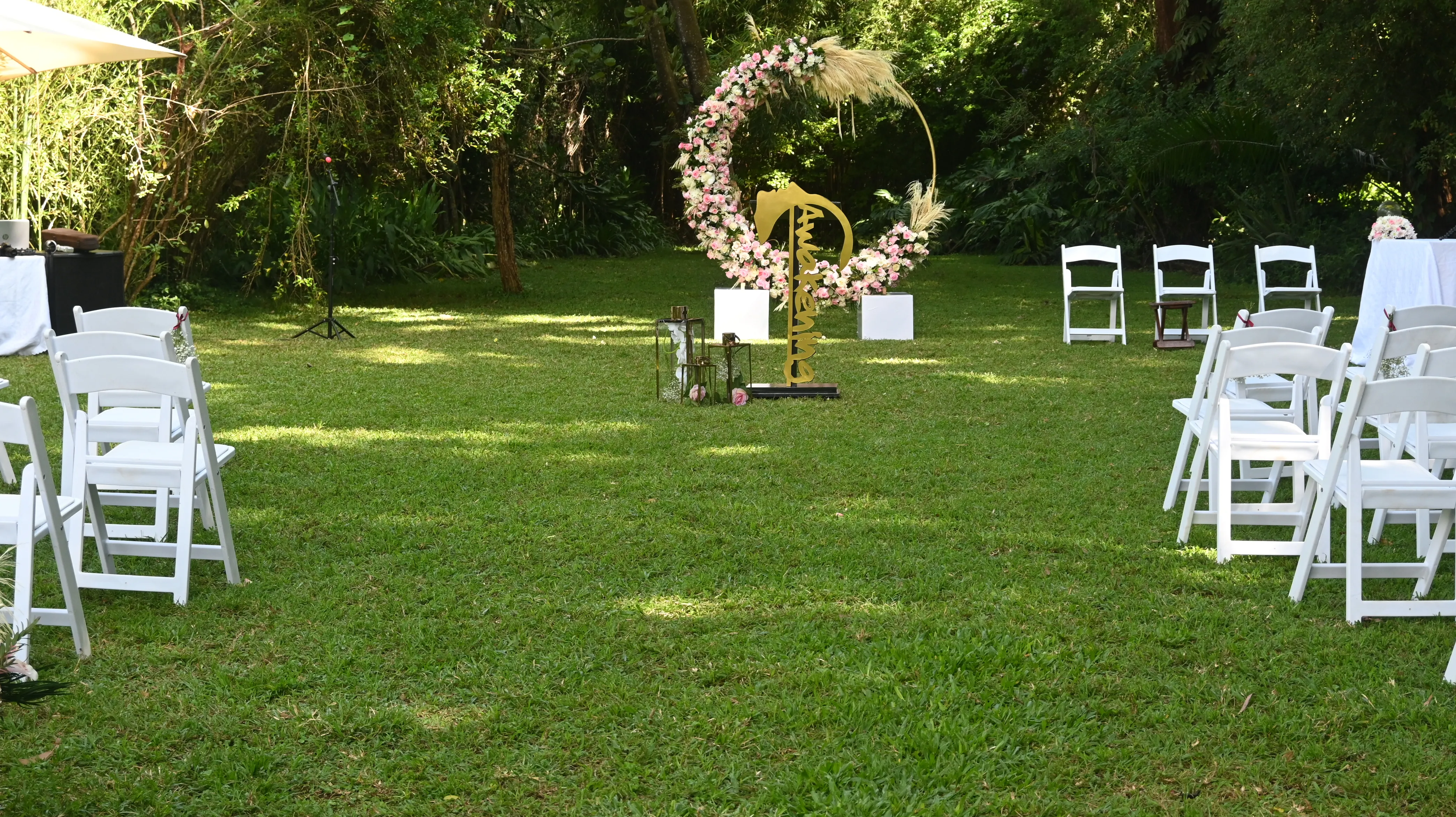 Outdoor garden wedding ceremony setup with white folding chairs facing a large circular floral arch capable of hosting signage.