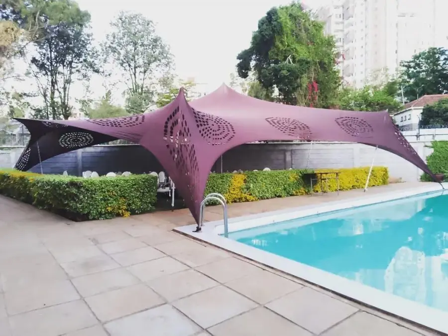 Deep purple stretch tent with decorative cutouts setup next to a swimming pool, contrasting with green hedges.
