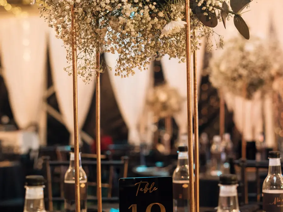 Eye-level view of a black, gold, and white table setting featuring a tall baby's breath centerpiece and a "Table 18" sign.