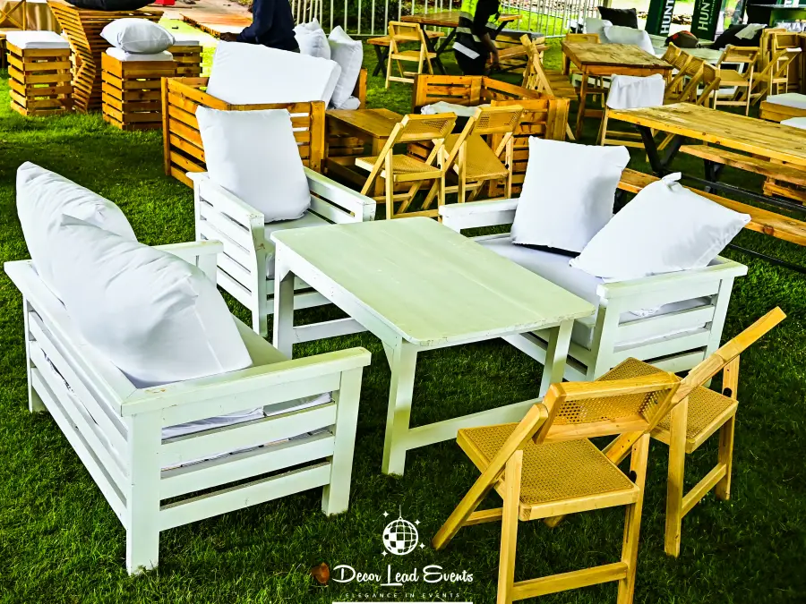 Outdoor lounge area featuring white pallet furniture with cushions and wooden folding chairs set up on the grass.