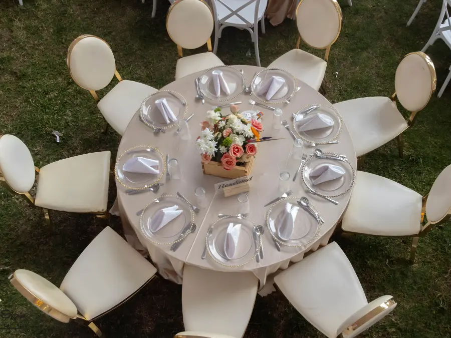 Overhead view of a round table with beige linen, peach floral centerpiece in a crate, and white chairs with gold rims.
