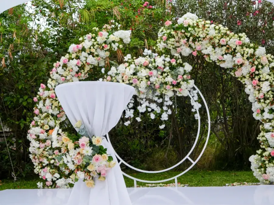 Decorative white stretch tent with cut-out patterns providing shade for a garden wedding altar with floral arches.