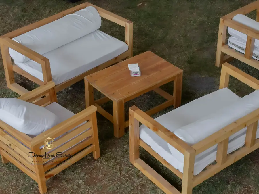 Aerial view of a rustic outdoor lounge area with wooden pallet sofas, white cushions, and a coffee table on the grass.